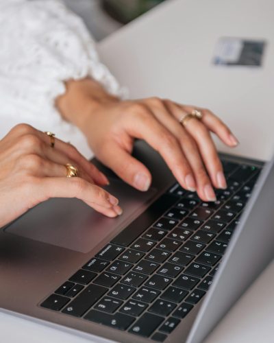 Hands of a woman typing on a laptop keyboard indoors, showcasing rings and fashion.